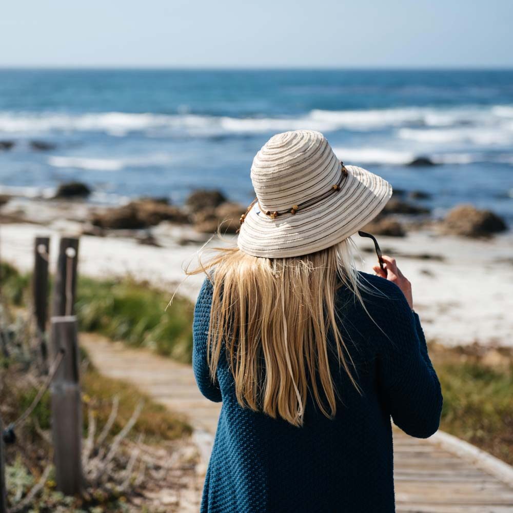 Blond woman wearing hat walking towards the sea